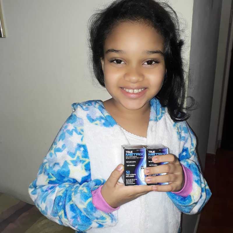 A Smiling Girl Holding Packaged 'True Metrix' Brand Glucometer Strips